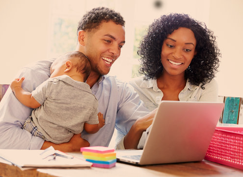 A women, and a man holding a baby working on a laptop